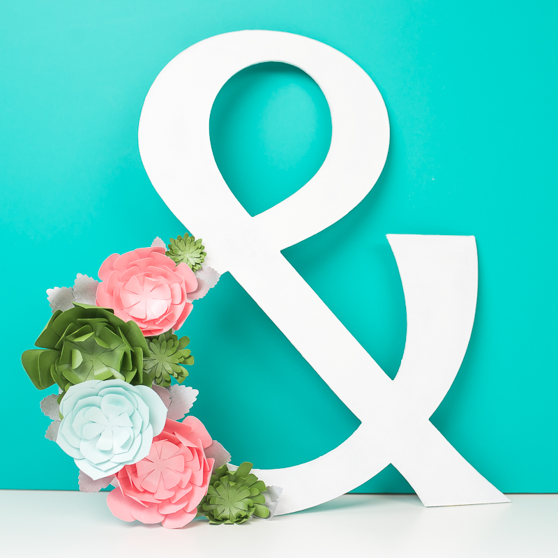 Full close-up image of a white ampersand decorated with colored paper succulents