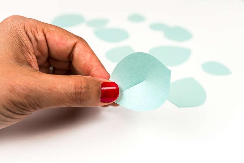 A close up of a person holding an aqua colored paper succulent with its end cut