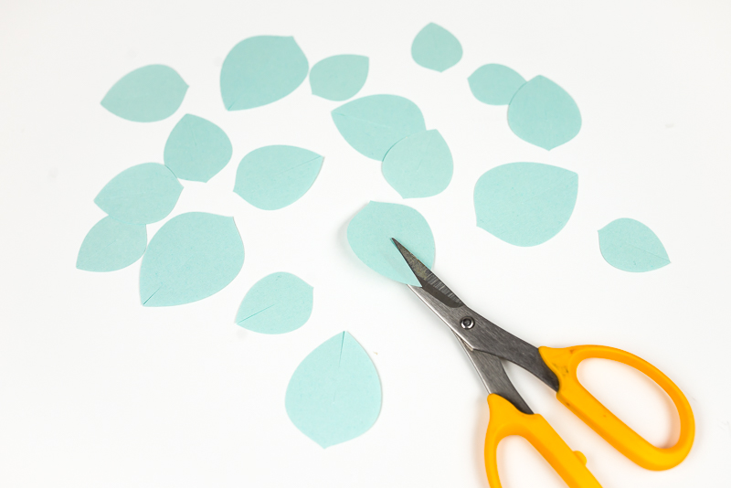 A scissors and images of several layers of an aqua colored paper succulent with cut ends