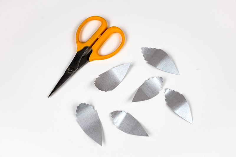 A scissors and images of several layers of a silver- colored paper leaves with curled ends